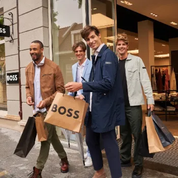 Vier Männer verlassen lachend den BOSS-Store im Designer Outlet Roermond während der Luxury Days, mit mehreren Einkaufstaschen in der Hand.