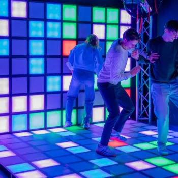 Drie mensen bewegen op een verlichte vloer met gekleurde vlakken in een donkere ruimte bij Poort51 in Weert