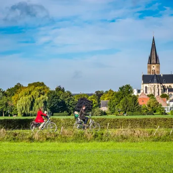 Fietsers in het landschap bij Thorn met uitzicht op de kerk en groene velden tijdens de Puzzelproeverij Maasvallei