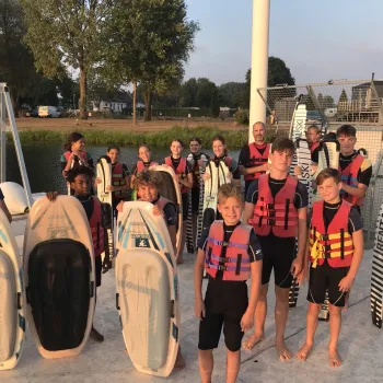 Kinderen en jongeren met zwemvesten, wakeboards en waterski’s tijdens een wakeboard- en waterski-activiteit van de Roermondse Sportzomer.