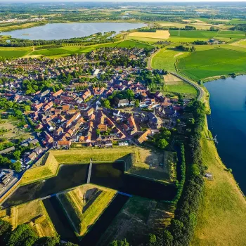 Luchtfoto van vestingstad Stevensweert met zicht op het Eiland in de Maas, omringd door water, groene velden en de Maasplassen in de verte.