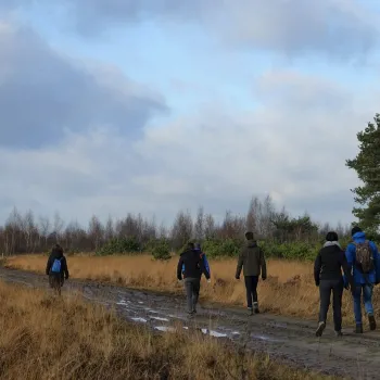 Deelnemers lopen tijdens de Turfstekerstocht over een modderig pad door open heide en grasland in Nationaal Park De Groote Peel.