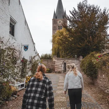 Twee vrouwen wandelen over een klinkerpad in het historische centrum van Thorn tijdens de VVV-wandeling Machtige Vrouwen van Thorn, met witte gevels, bloeiende tuinen en de kerktoren op de achtergrond.