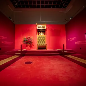De rijkversierde Nederlandse troon met gouden details staat centraal in een rode tentoonstellingsruimte van het Cuypershuis in Roermond.