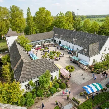 Zonnige luchtfoto van de voorjaarsfair op de binnenplaats van Kasteel Daelenbroeck, met veel groen, bloemen en gestreepte marktkraampjes waar mensen tussendoor wandelen.