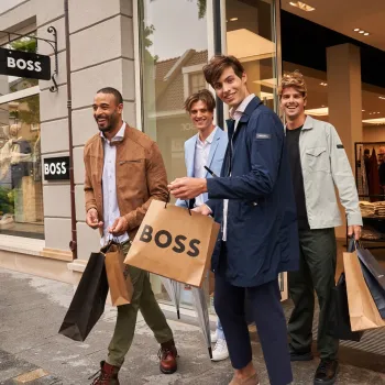 Vier Männer mit Einkaufstaschen verlassen lachend das BOSS-Geschäft während der Wintersale im Designer Outlet Roermond.