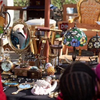 Kraam met vintage spullen, lampen en spiegels tijdens de rommelmarkt op de Zomerfeesten Beegden, met bezoekers op de voorgrond.